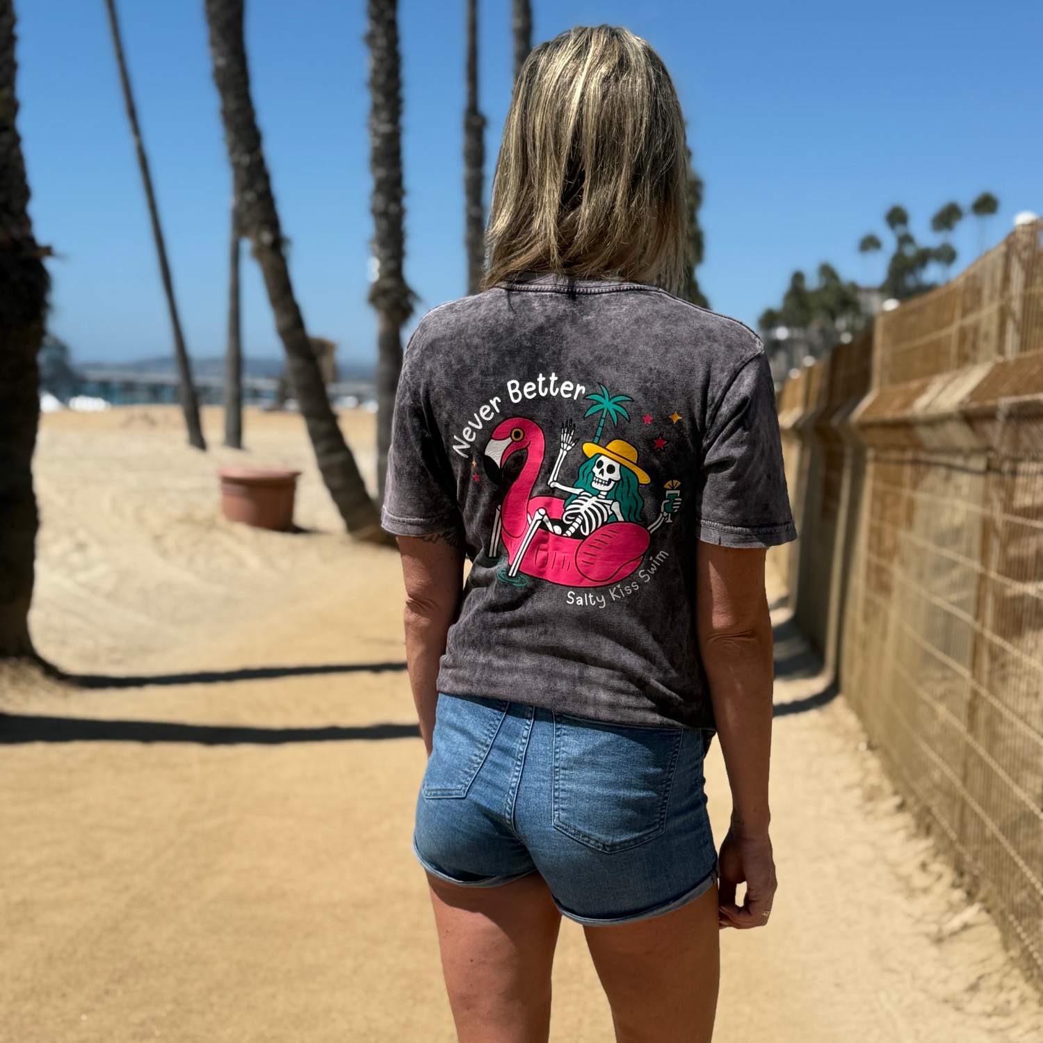 Person wearing a t-shirt with a flamingo graphic and text, standing on a beach.