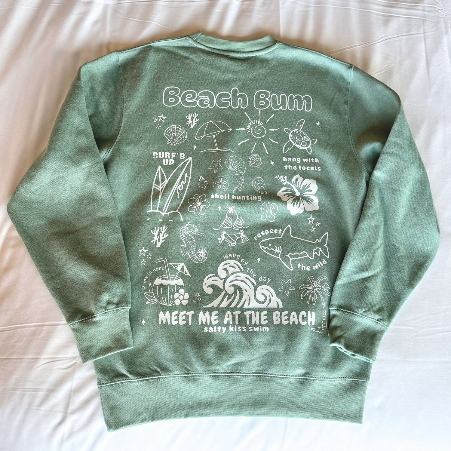 Green sweatshirt with beach-themed graphics and text on a light background