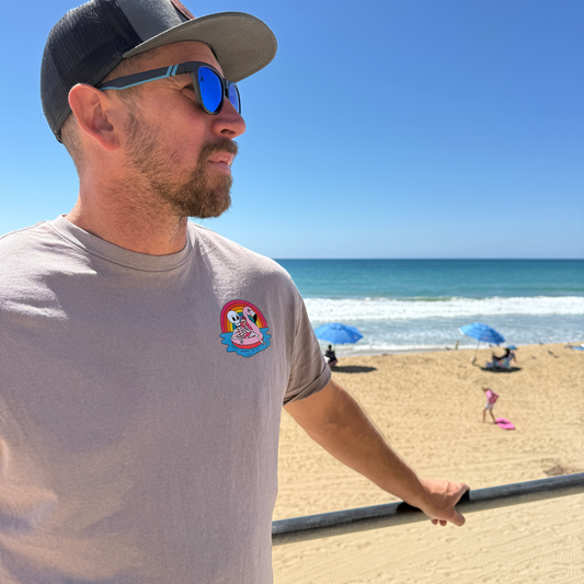 Man wearing sunglasses and a cap on a beach with blue sky and ocean.